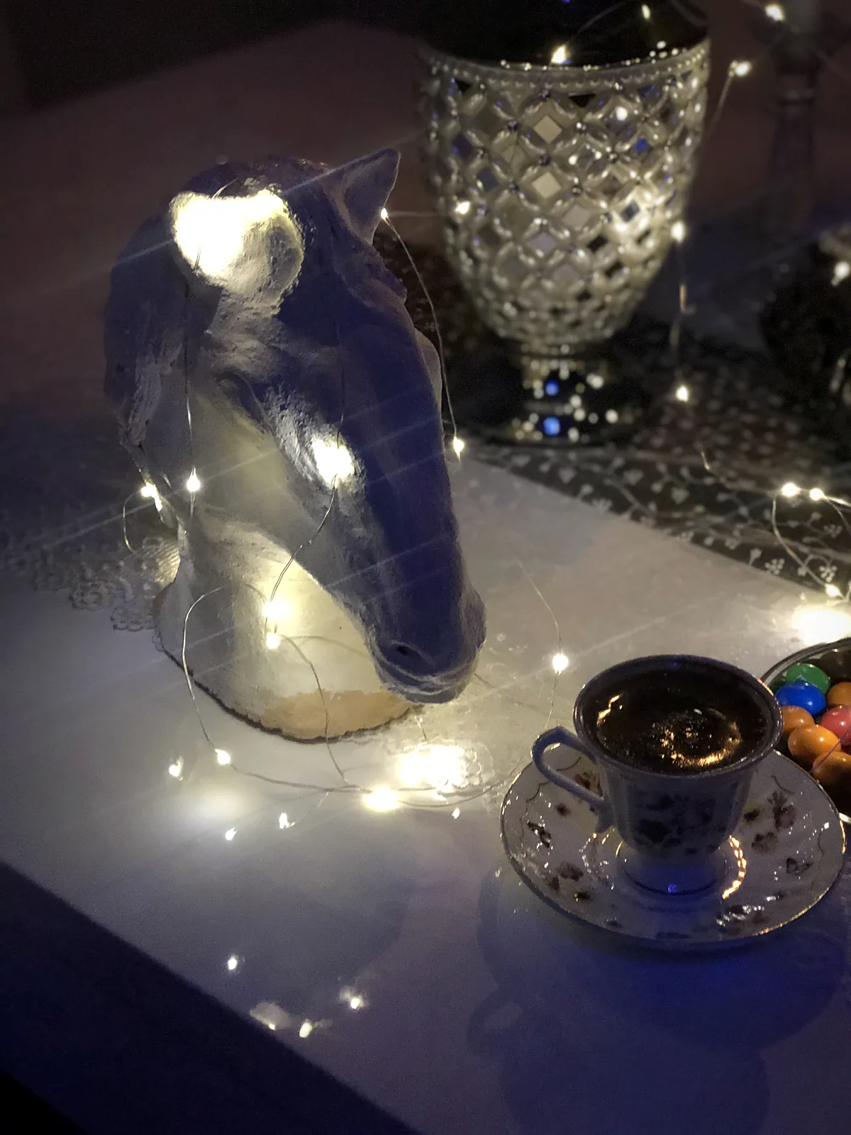 Peri ışıkları arasında el yapımı at başı heykeli ve bir fincan Türk kahvesi